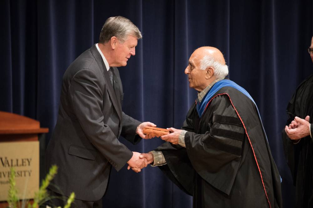 President Emeritus Haas shaking hands and passing over a milestone award to a faculty member.